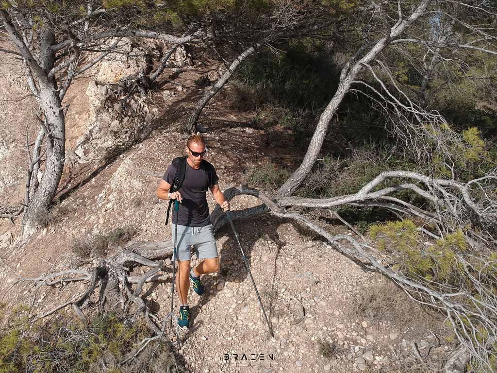 Young hiker descending hill in woods with trekking poles